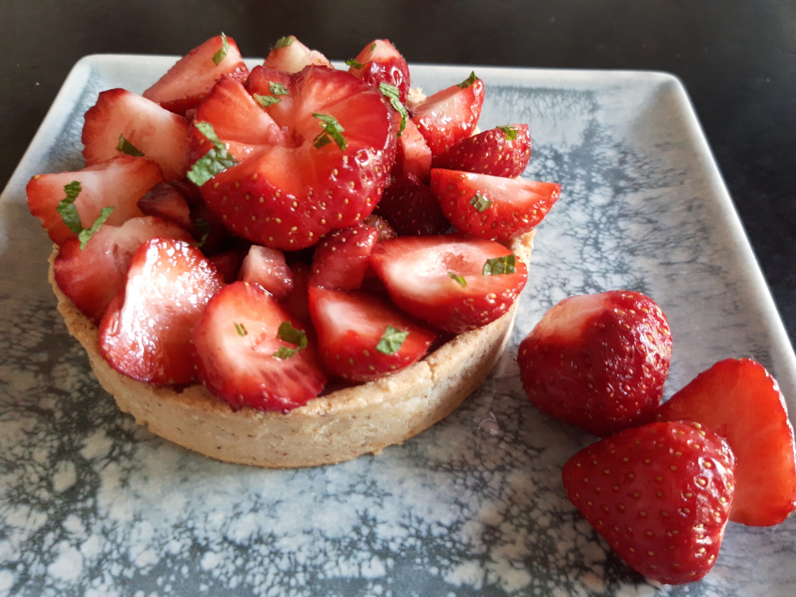 Tarte aux fraises sur une assiette, avec quelques fraises en décoration