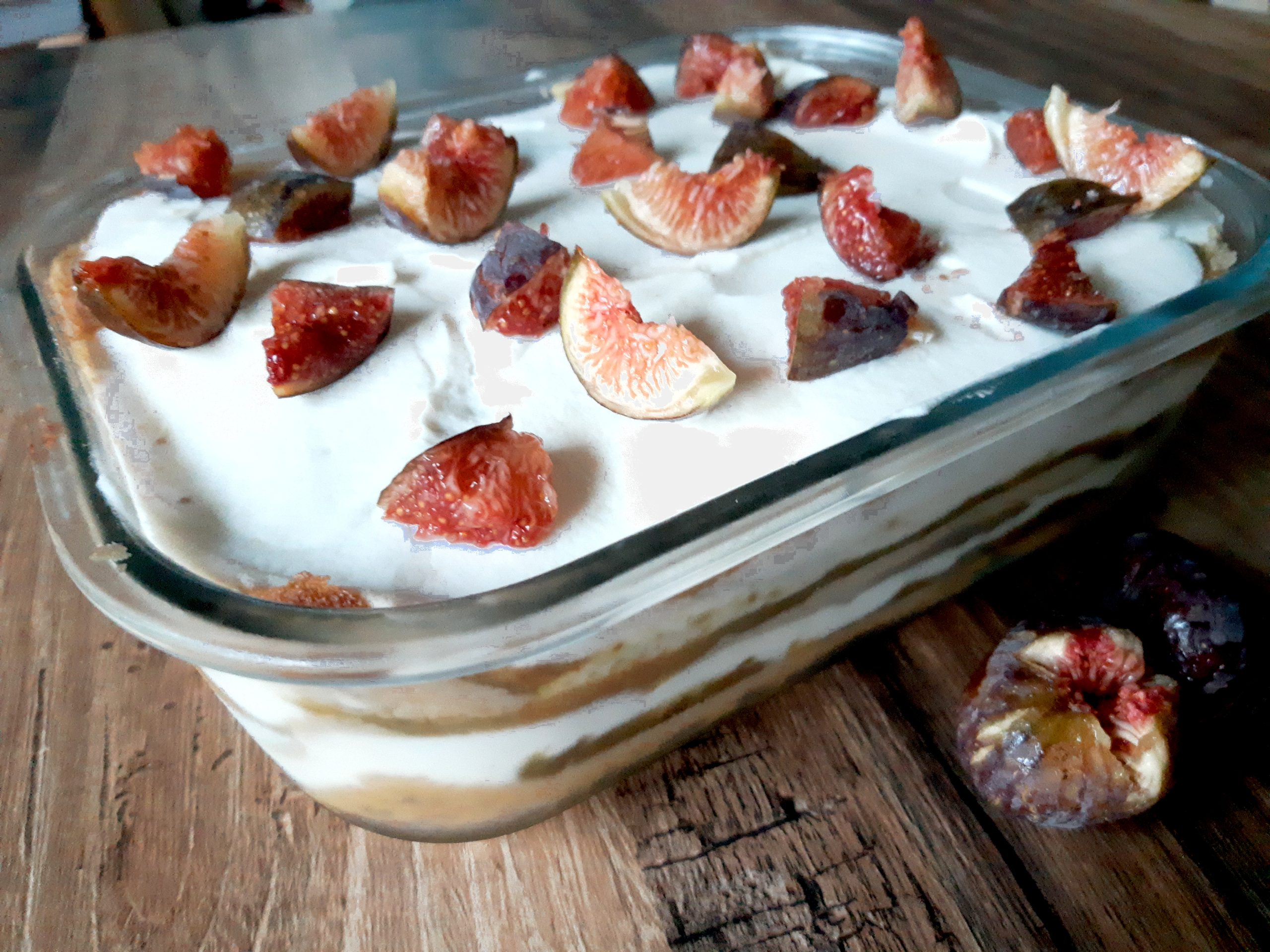 Tiramisu végétal dans un grand plat en verre posé sur un support en bois. Des quartiers de figues fraîches décorent ce tiramisu.